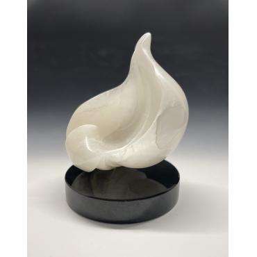 Spirited by Elisa Adams, a 13" by 11" Italian Alabaster sculpture. A smooth, abstract white sculpture resembling a flame or teardrop, set on a black circular base.