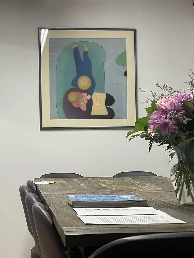 A meeting room with a wooden table and chairs. On the wall hangs an abstract painting of two faceless figures.