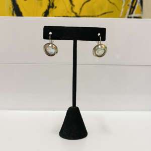 Silver round earrings with gemstones displayed on a black stand, set against a white and yellow abstract background.