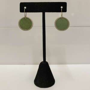 A pair of round green coconut shell earrings with silver rims are displayed on a black stand.