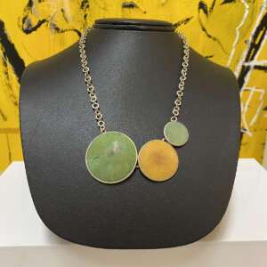 A necklace with three circular pendants in green and yellow hues on a black display stand.