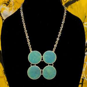 A necklace with four round turquoise stones set in a square formation is displayed on a black bust.