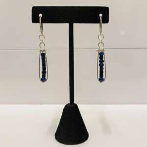 Silver drop earrings with dark blue beads, displayed on a black velvet stand against a plain background.