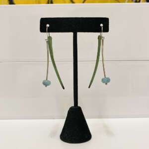 Elegant drop earrings hang on a black stand. Each earring features a curved green stem and a quartz bead, set against a plain backdrop.