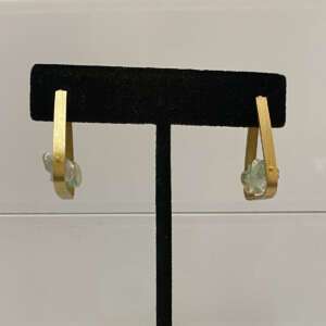 Vermeil triangular earrings with light green gemstones hang on a black stand.